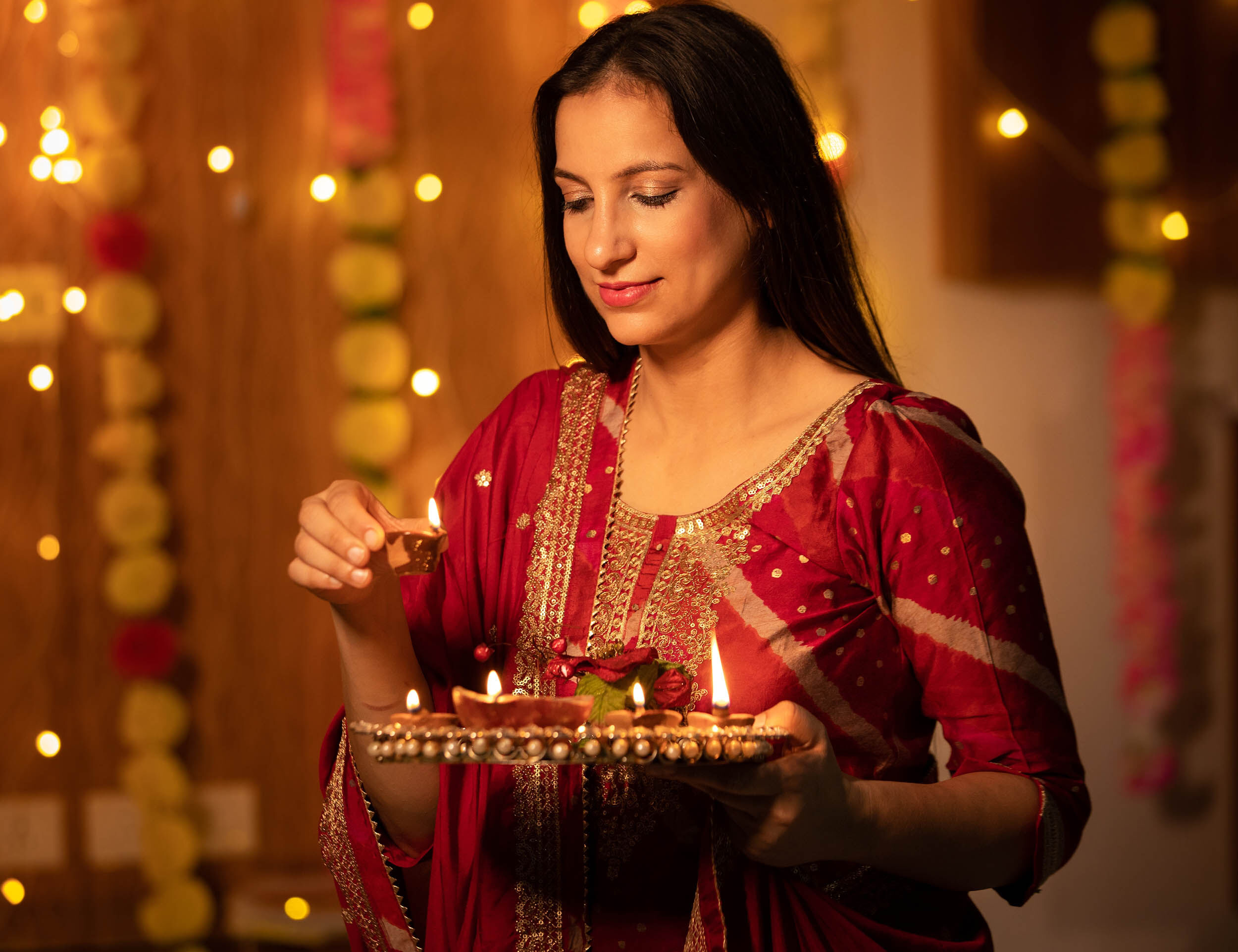 A woman in a traditional outfit lighting diyas, a beautiful part of Diwali celebrations.
